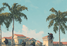 Part I — The Gate That Forgot It Was a Gate Three figures with backpacks are depicted climbing over a tall black metal fence and an adjacent stone pillar to enter a large, upscale house with a red tile roof and palm trees under a bright sky.